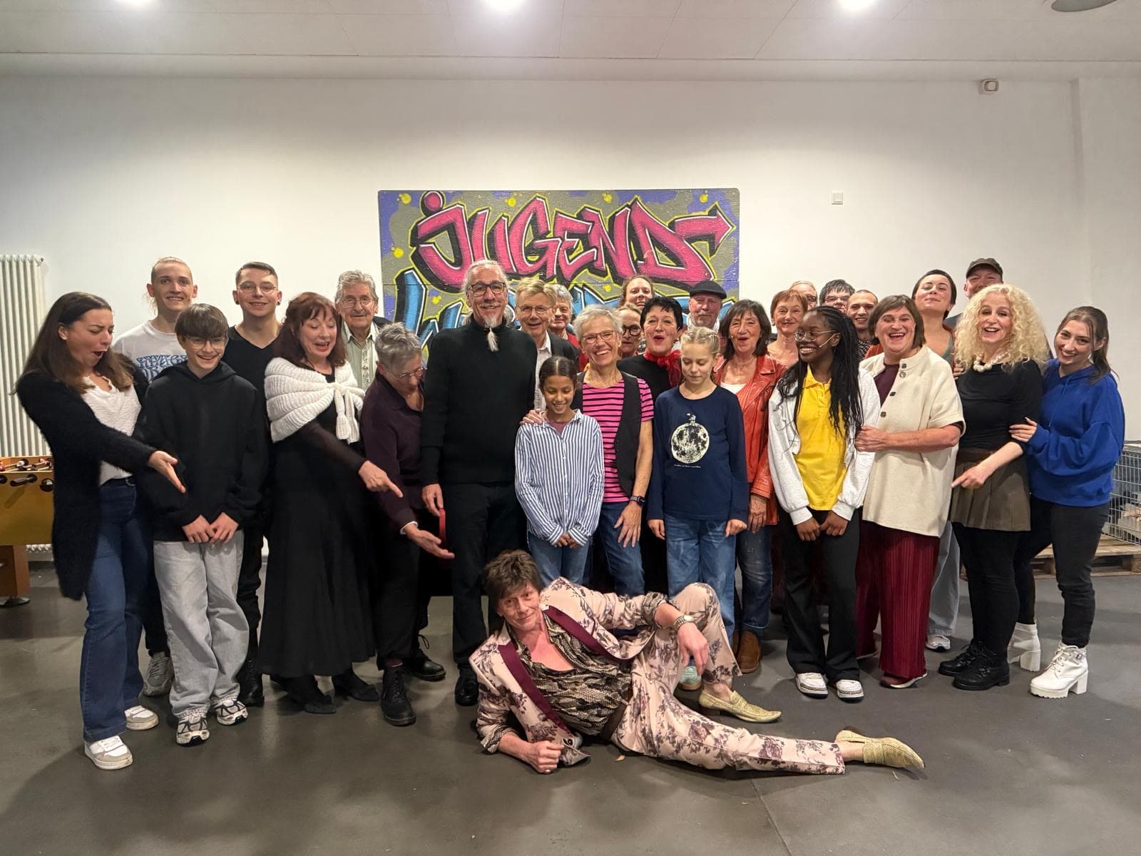 Ein Gruppenfoto der Akteure eines Theaterstücks. Es sind 29 Personen unterschiedlichen Alters auf dem Foto, alle lachen.