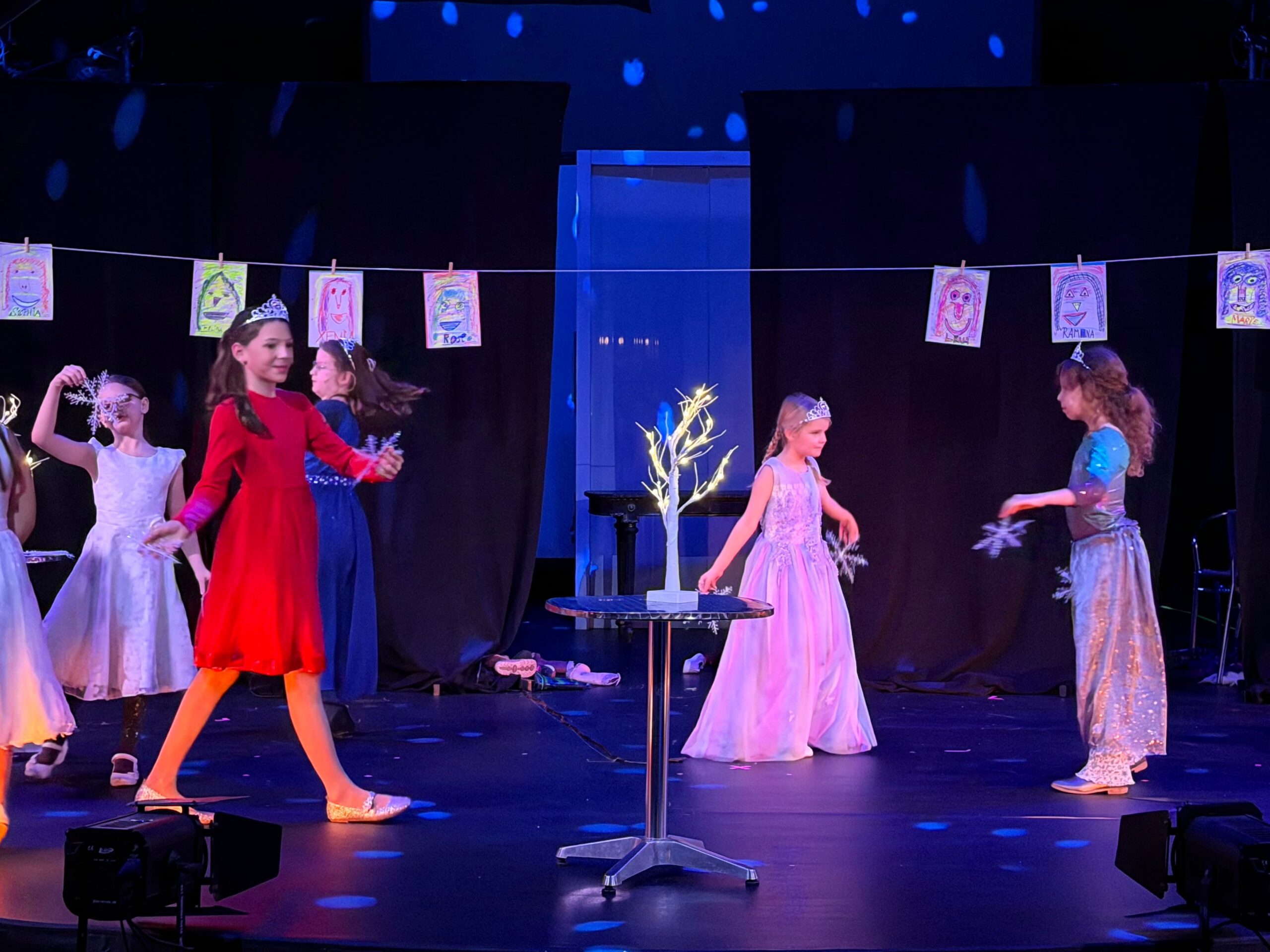 Viele Mädchen als Prinzessin verkleidet laufen mit großen Schneeflocken über eine dunkle Bühne.