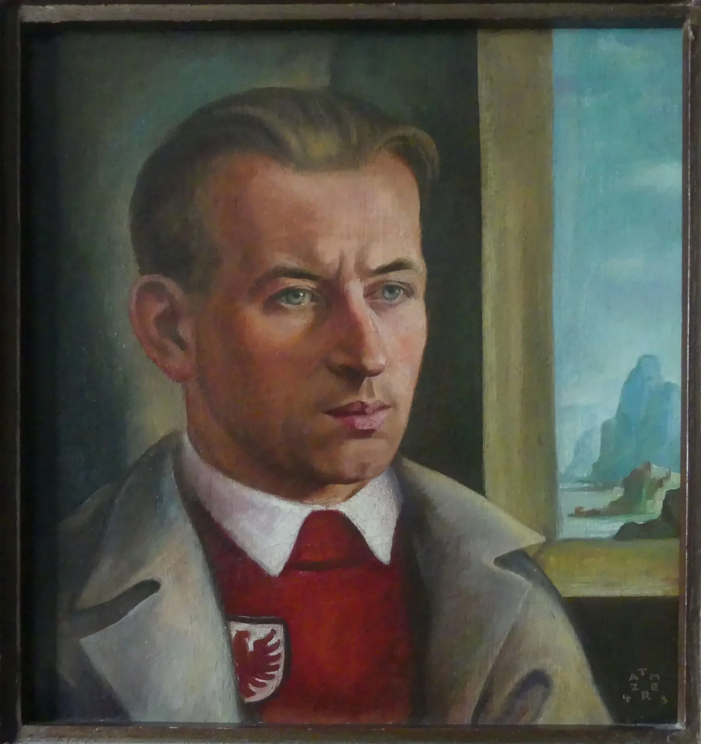 Ein Mann mit hellem Haar, der einen beigen Mantel und einen roten Pullover mit einem weißen Emblem trägt, sitzt drinnen und blickt zur Seite. Durch ein Fenster hinter ihm ist eine Landschaft mit Wasser, Felsen und Himmel zu sehen.