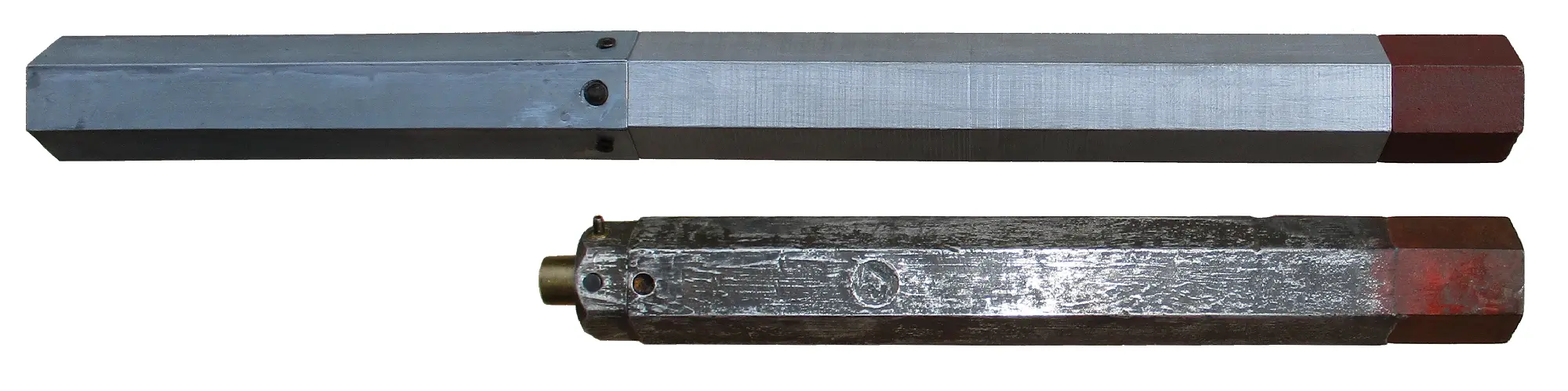 Zwei metallene sechseckige Stangen mit rot lackierten Enden, die übereinander angeordnet sind; die obere Stange wirkt neuer und glatter, während die untere Stange älter und abgenutzter aussieht, mit sichtbarer Struktur und einer Messingbeschlag.