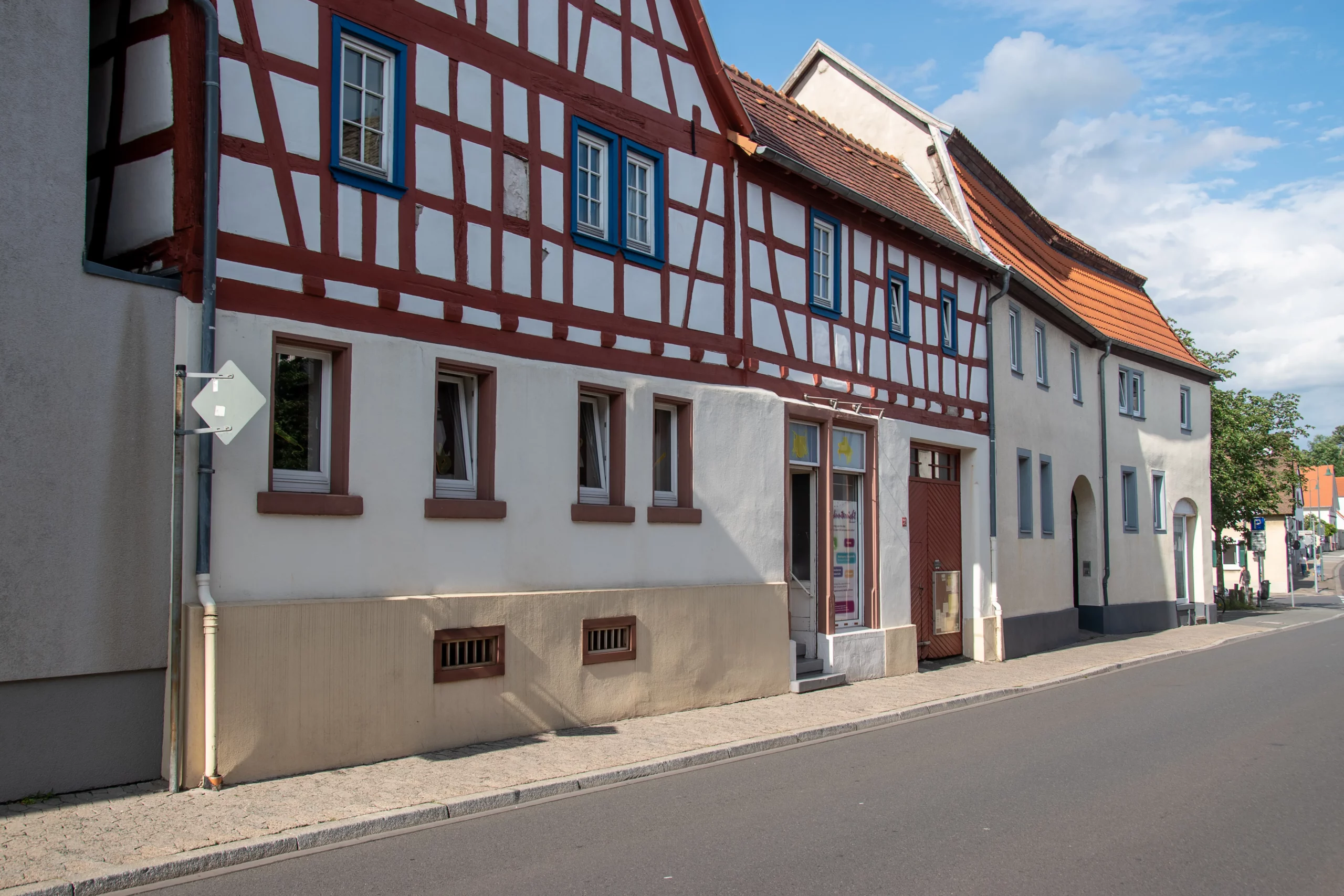 Eine ruhige Straße mit traditionellen Fachwerkhäusern, die an einem sonnigen Tag mit weißen Wänden, roten Balken und blau umrandeten Fenstern bestechen.