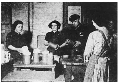Schwarz-Weiß-Foto von vier Personen, die in einem schlichten Innenraum um einen Tisch herum Essen in Metallbehälter füllen; einige tragen Schürzen oder Uniformen.